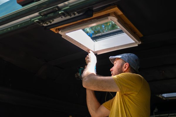 Handyman using a cordless drill while installing a camper van roof window
